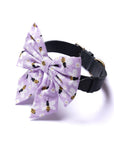 Dog collar with a large purple bow featuring bee patterns on a white background