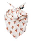 A baby bandana-style pet collar in cream with a repeating print of orange-brown teddy bears, tied at the top with a small black brand tag reading 'THE Paws'.