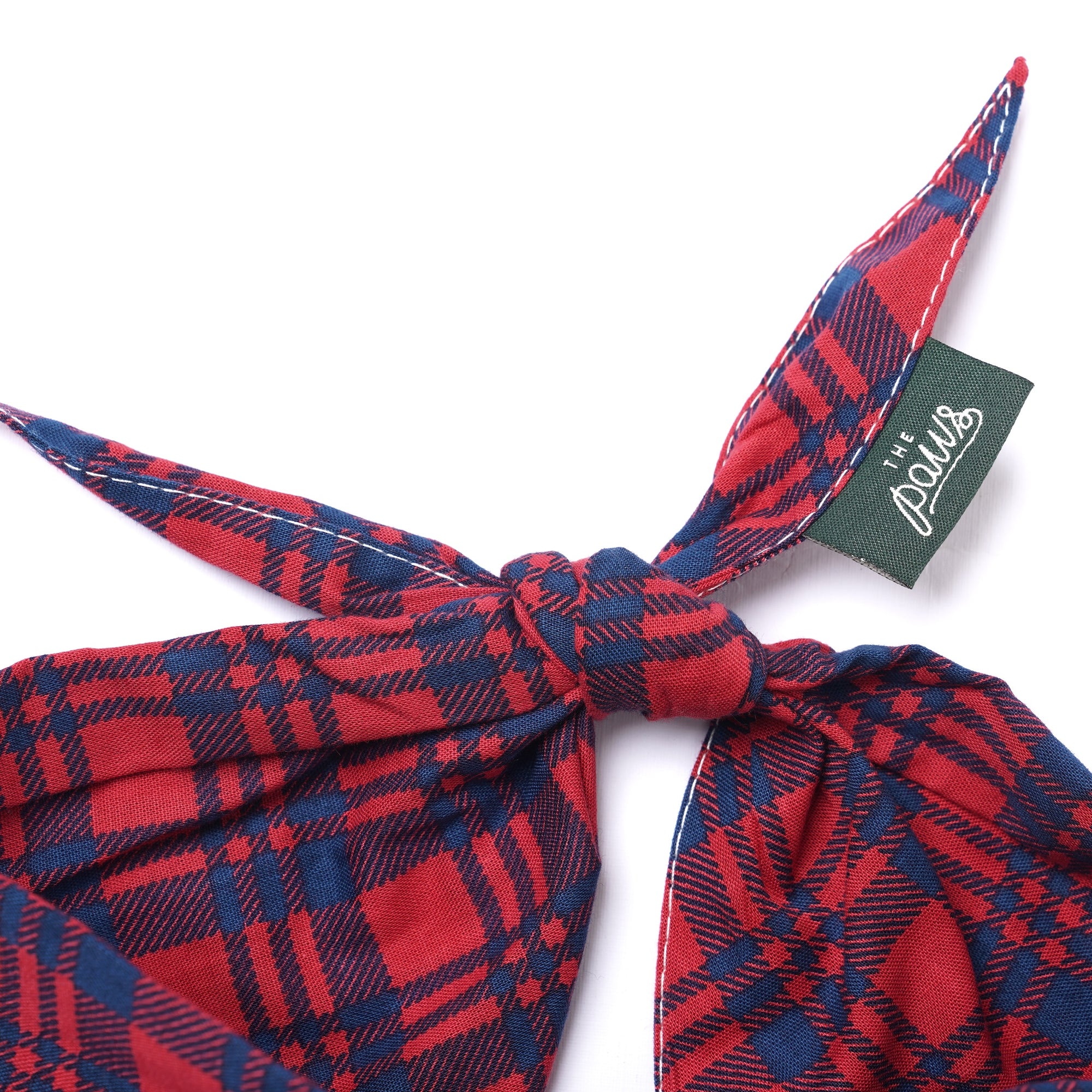 Red and blue plaid dog bandana with a knot and a brand tag on a white background