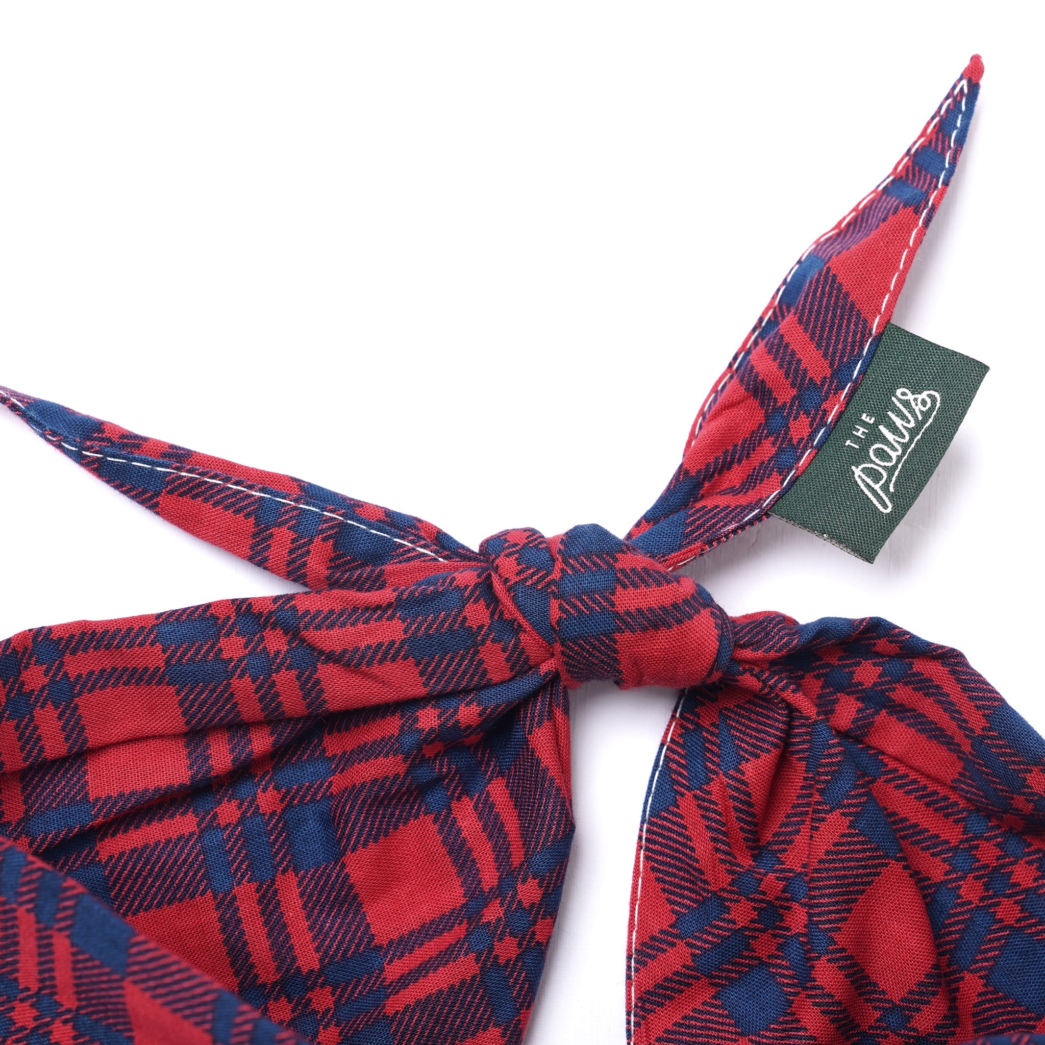 Red and blue plaid dog bandana with a knot and a brand tag on a white background