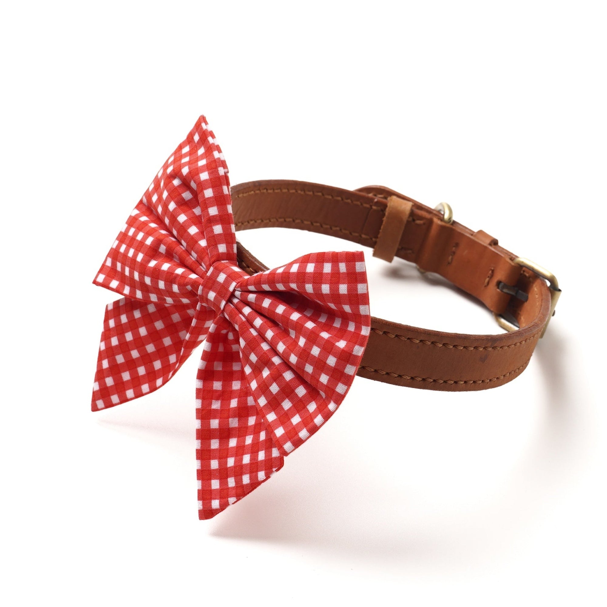 A red gingham bow tie with a sailor bow design, attached to a brown leather collar.