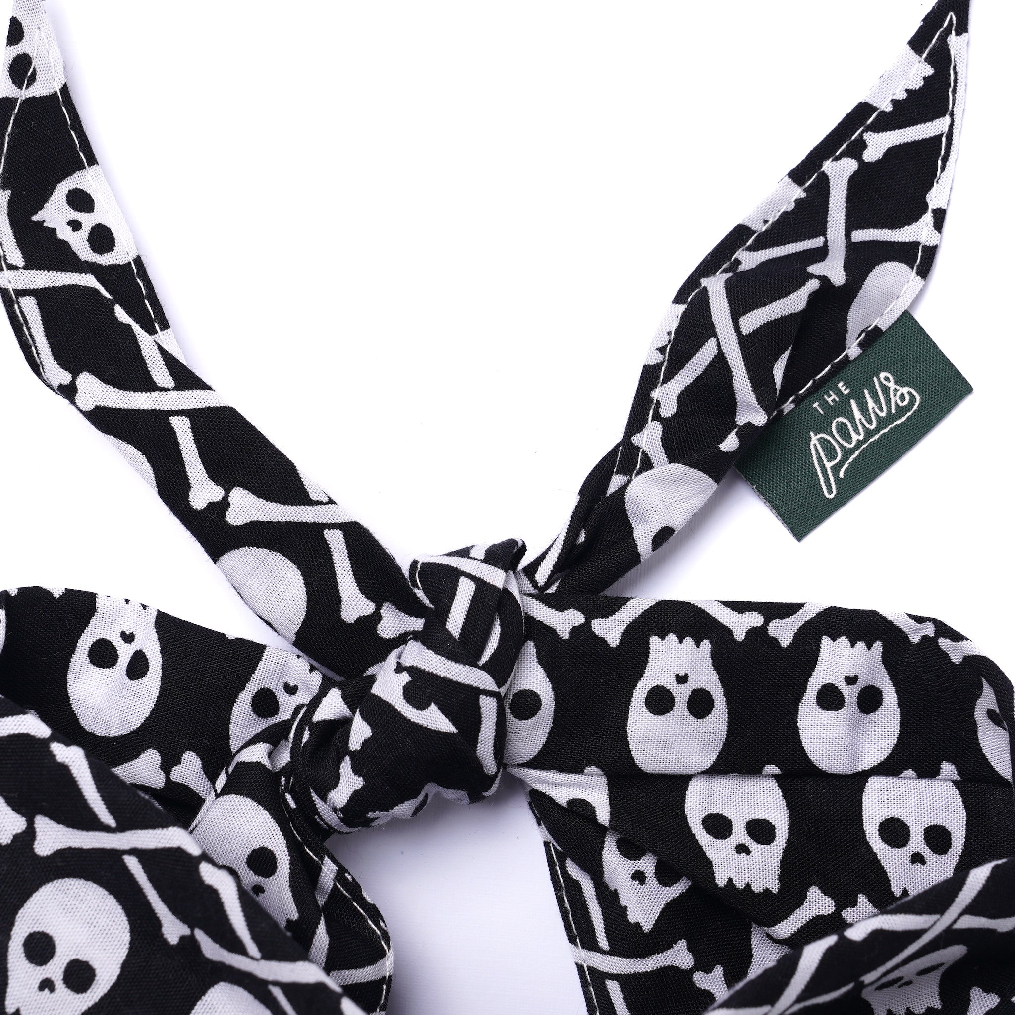 Black and white skull and bone patterned dog bandana with a visible brand tag on a white background